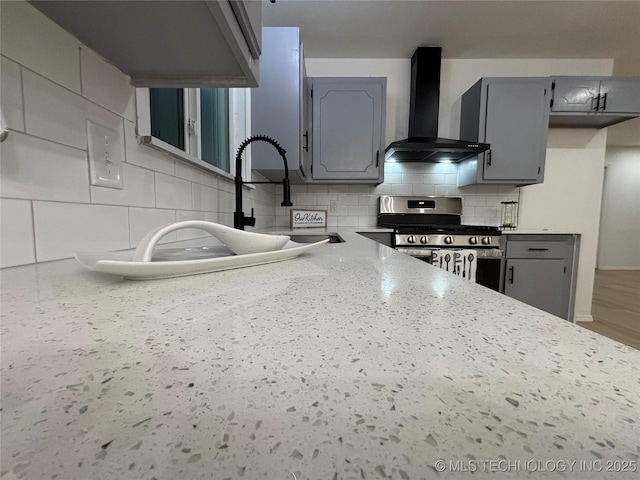 kitchen with wall chimney range hood, gray cabinets, and gas stove