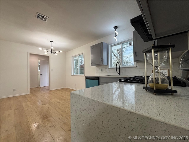 kitchen featuring tasteful backsplash, a notable chandelier, dishwasher, light stone countertops, and sink