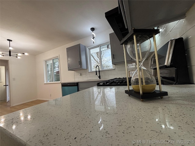 kitchen featuring dishwashing machine, decorative backsplash, sink, a chandelier, and light stone counters