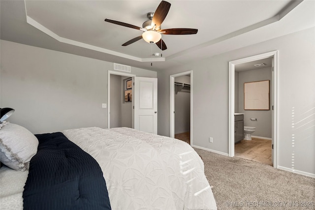 carpeted bedroom featuring ensuite bath, a spacious closet, a raised ceiling, a closet, and ceiling fan