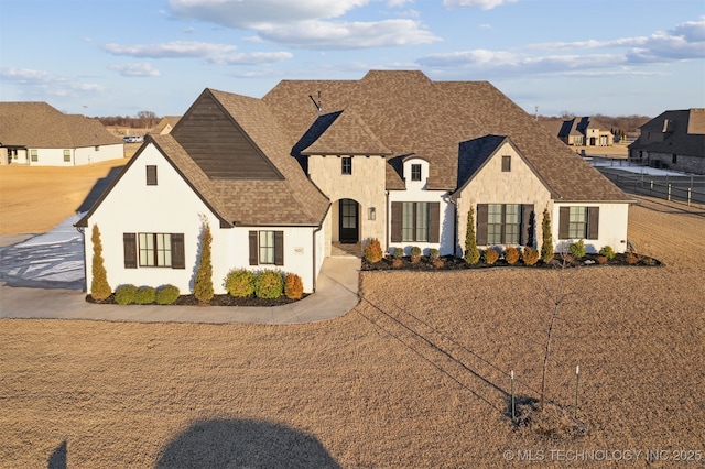 french country home featuring fence, roof with shingles, and stucco siding