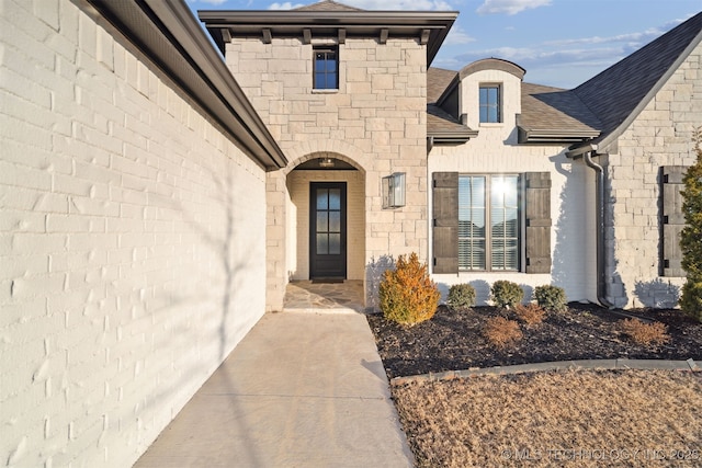 property entrance with stone siding and a shingled roof