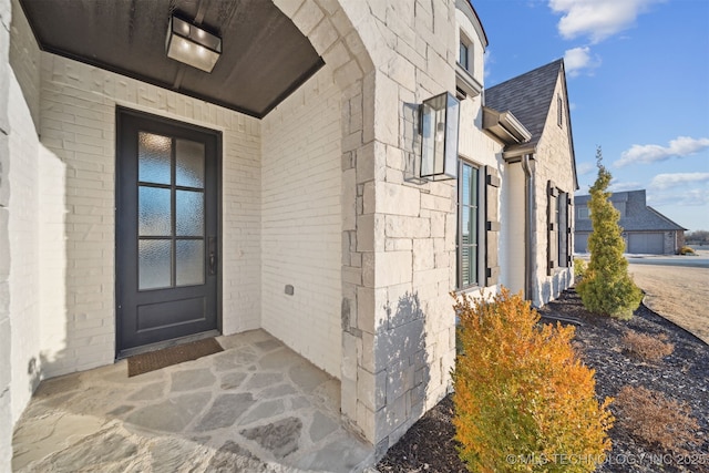view of exterior entry featuring brick siding and roof with shingles