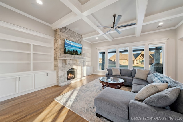 living room featuring beamed ceiling, ceiling fan, light hardwood / wood-style flooring, built in shelves, and a stone fireplace