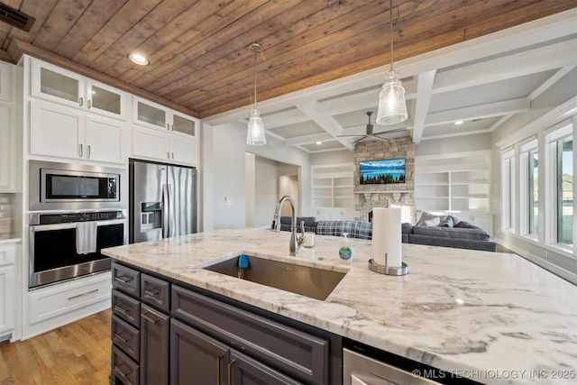 kitchen with light stone countertops, hanging light fixtures, stainless steel appliances, white cabinetry, and sink