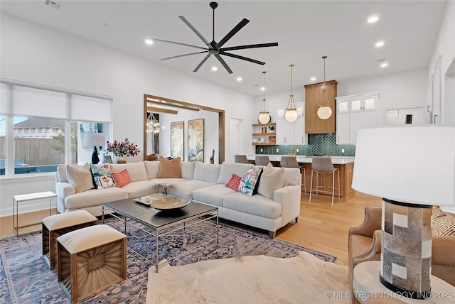 living room featuring light wood-type flooring, ceiling fan with notable chandelier, and a wealth of natural light