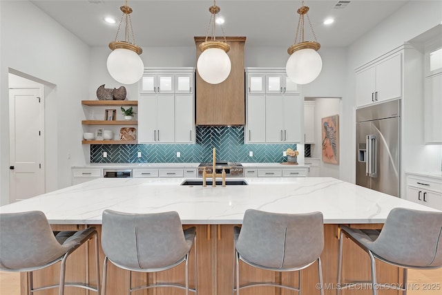 kitchen featuring built in fridge, an island with sink, white cabinetry, and pendant lighting