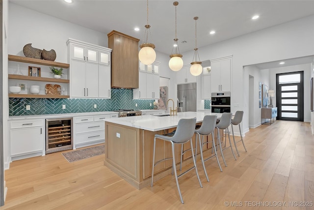 kitchen with a large island with sink, white cabinets, wine cooler, and appliances with stainless steel finishes