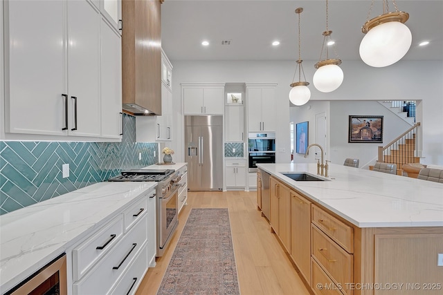 kitchen featuring white cabinets, decorative light fixtures, sink, a center island with sink, and high quality appliances