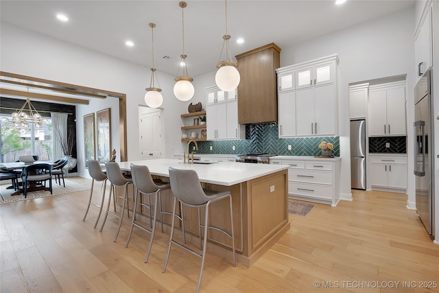 kitchen featuring hanging light fixtures, white cabinets, a kitchen island with sink, range, and high end refrigerator