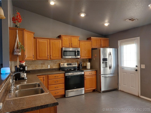 kitchen featuring lofted ceiling, sink, a textured ceiling, tasteful backsplash, and stainless steel appliances