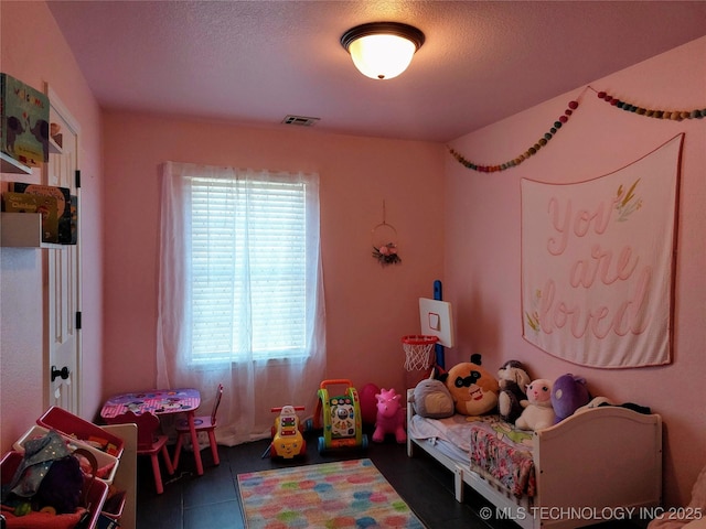 playroom with a textured ceiling, dark tile patterned flooring, and a healthy amount of sunlight