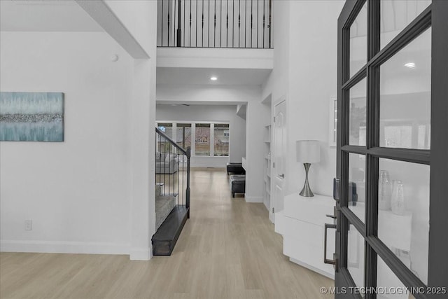 hall featuring light hardwood / wood-style flooring and a towering ceiling