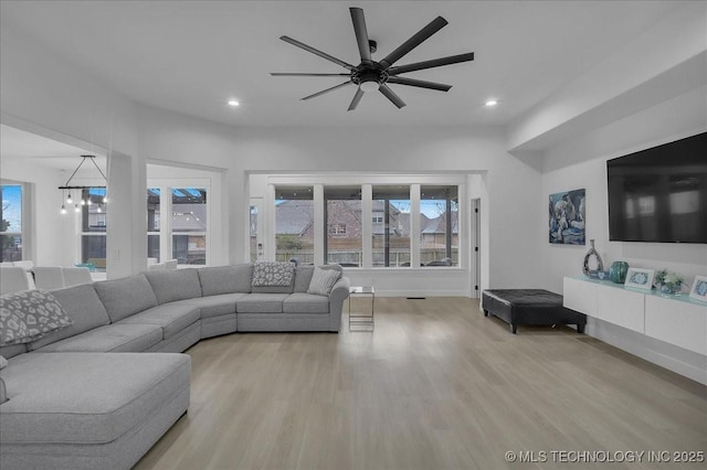 living room featuring ceiling fan with notable chandelier and light hardwood / wood-style flooring