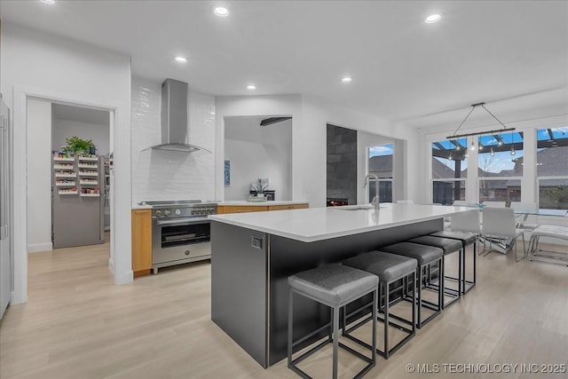 kitchen featuring wall chimney exhaust hood, a center island with sink, tasteful backsplash, stainless steel range, and sink