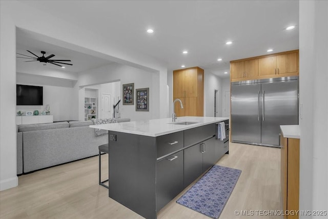 kitchen featuring stainless steel built in refrigerator, sink, ceiling fan, light hardwood / wood-style floors, and an island with sink