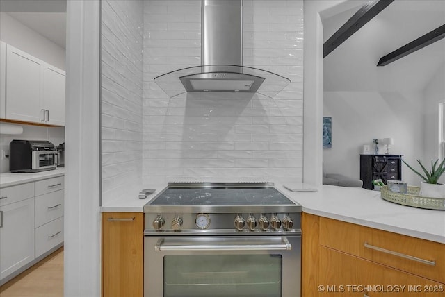 kitchen with high end stainless steel range, white cabinets, wall chimney range hood, and decorative backsplash