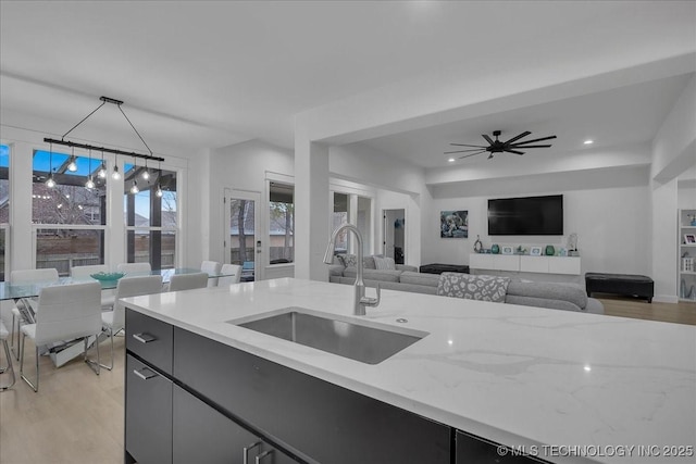 kitchen featuring hanging light fixtures, ceiling fan, light stone counters, sink, and light hardwood / wood-style flooring