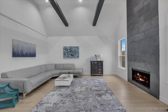 living room featuring beam ceiling, light hardwood / wood-style floors, a tile fireplace, and high vaulted ceiling