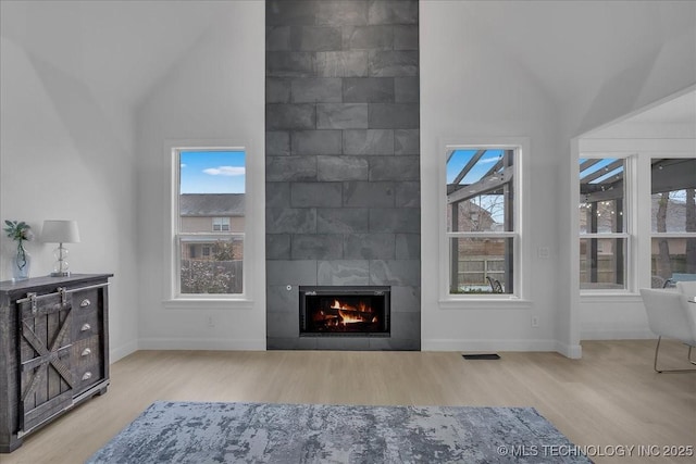 living room with light hardwood / wood-style flooring, a tile fireplace, and vaulted ceiling