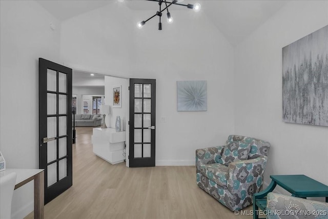 sitting room with light hardwood / wood-style floors, french doors, lofted ceiling, and a notable chandelier