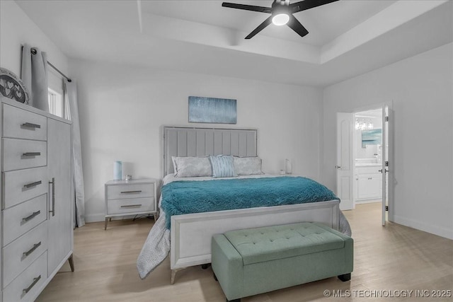 bedroom with ceiling fan, light wood-type flooring, ensuite bath, and a tray ceiling