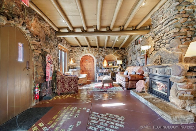 interior space with beam ceiling, a stone fireplace, wood ceiling, and wooden walls