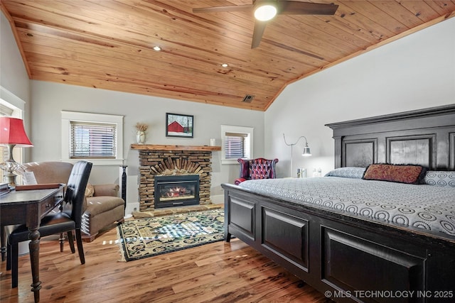 bedroom featuring light wood-type flooring, wood ceiling, vaulted ceiling, ceiling fan, and a stone fireplace