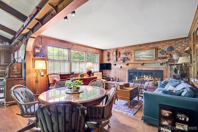 dining space with beam ceiling, light hardwood / wood-style flooring, brick wall, wooden walls, and a fireplace