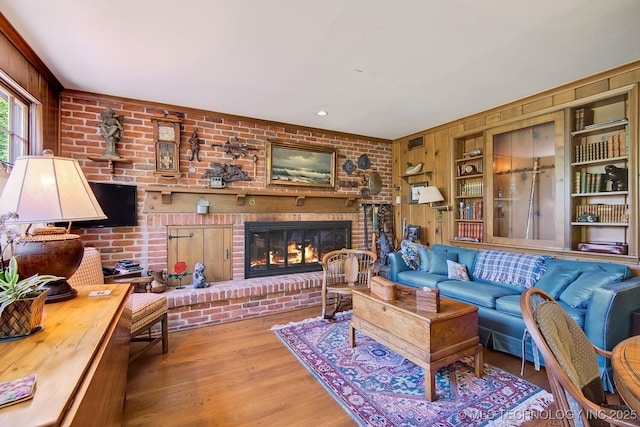 living room featuring built in shelves, wood walls, wood-type flooring, and a fireplace