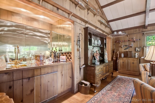 bar featuring wooden walls, sink, lofted ceiling with beams, and hardwood / wood-style flooring