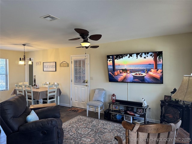 living room featuring ceiling fan with notable chandelier, a wood stove, and dark wood-type flooring