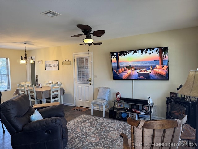 living room featuring ceiling fan with notable chandelier, dark hardwood / wood-style flooring, and a wood stove