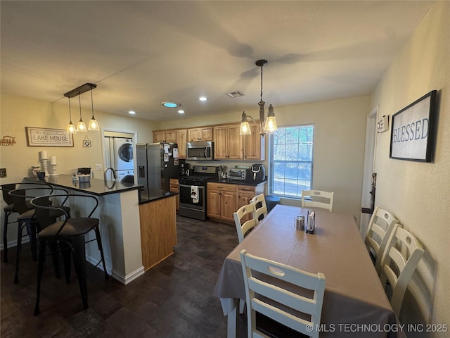 kitchen featuring a kitchen bar, appliances with stainless steel finishes, pendant lighting, and stacked washer / drying machine