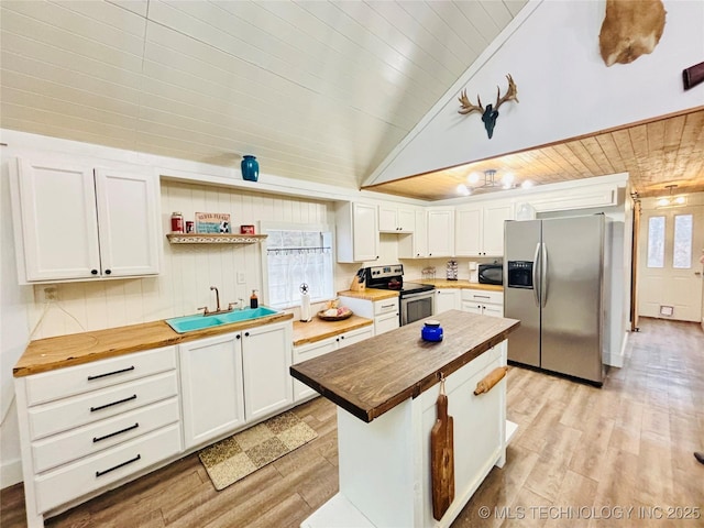 kitchen featuring stainless steel appliances, white cabinetry, butcher block counters, and a wealth of natural light