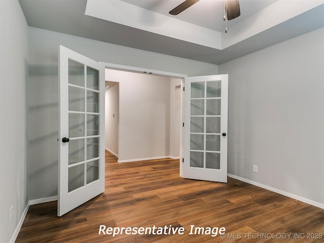 unfurnished room with a raised ceiling, ceiling fan, french doors, and dark wood-type flooring