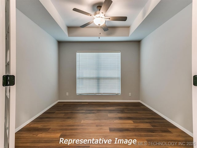 spare room featuring a tray ceiling, ceiling fan, and dark wood-type flooring