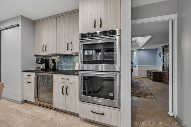 kitchen with light brown cabinetry, light tile patterned floors, beverage cooler, double oven, and a barn door