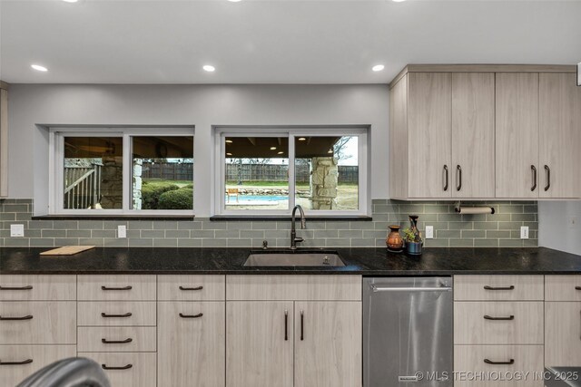 kitchen featuring dark stone countertops, sink, stainless steel dishwasher, and light brown cabinets