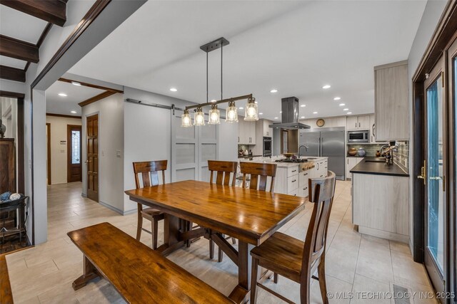 tiled dining space with ornamental molding, a barn door, sink, and beam ceiling