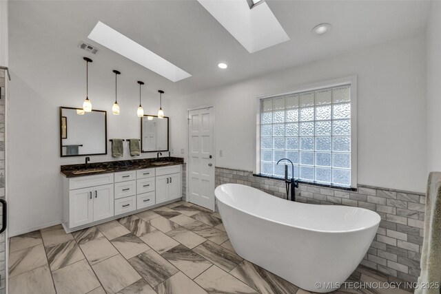 bathroom featuring tile walls, vanity, a skylight, and a tub