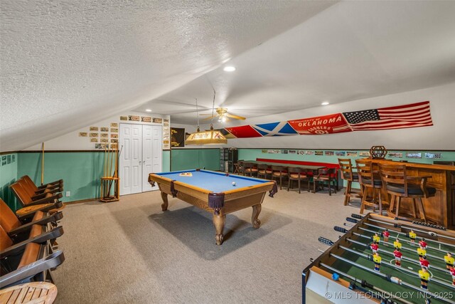 recreation room featuring carpet flooring, bar area, vaulted ceiling, and a textured ceiling