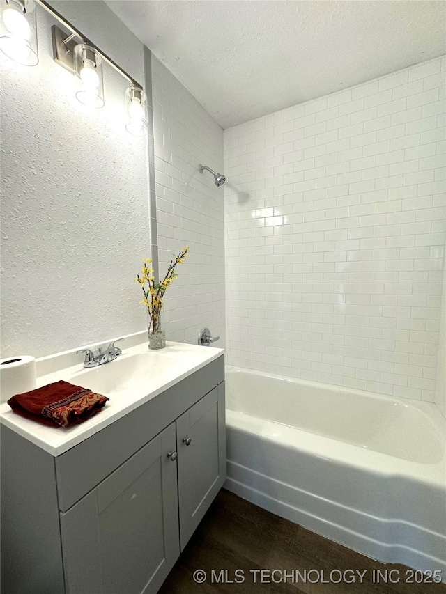 bathroom with a textured ceiling, tiled shower / bath, wood-type flooring, and sink