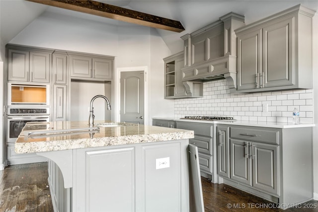 kitchen featuring gray cabinets, appliances with stainless steel finishes, an island with sink, dark hardwood / wood-style floors, and backsplash