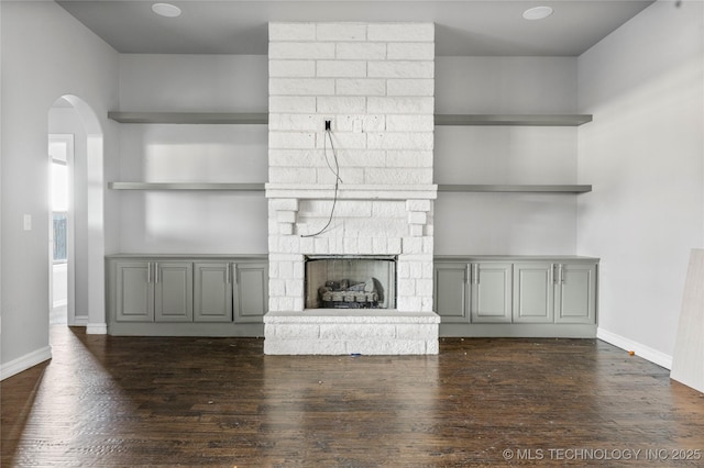 unfurnished living room with built in shelves, dark hardwood / wood-style flooring, and a stone fireplace