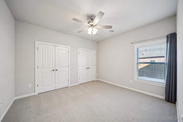 unfurnished bedroom featuring ceiling fan, light carpet, and multiple closets