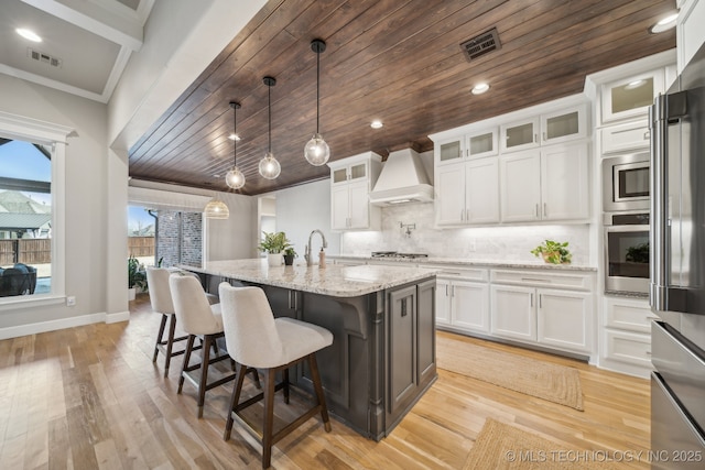 kitchen with pendant lighting, a center island with sink, white cabinets, custom range hood, and appliances with stainless steel finishes