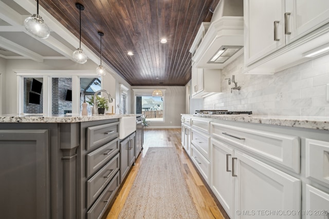 kitchen featuring backsplash, light wood-type flooring, custom range hood, decorative light fixtures, and white cabinetry