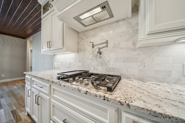 kitchen featuring stainless steel gas stovetop, backsplash, light hardwood / wood-style flooring, light stone countertops, and white cabinetry