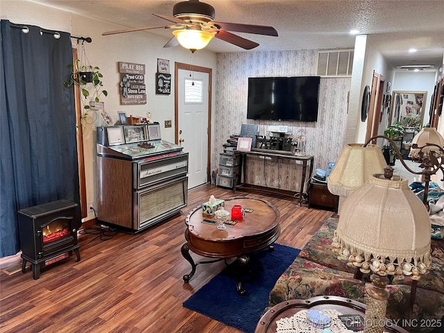 living room featuring hardwood / wood-style floors, ceiling fan, a wood stove, and a textured ceiling